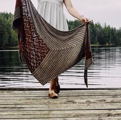 a woman is holding a blanket over her head while standing on a dock by the water