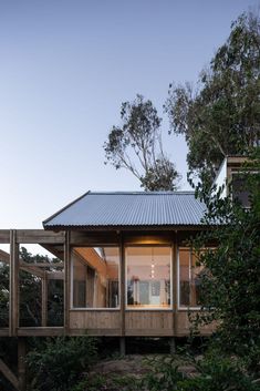 a small wooden cabin in the woods with glass walls and metal roofing on top