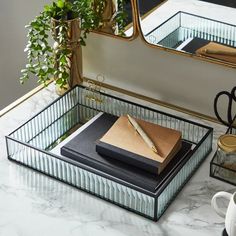 a desk with a mirror, pen and notebook on it in front of a plant