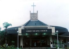 a church with a cross on the roof and people walking in front at the entrance