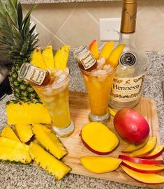 pineapples, mangoes, and rum are on a cutting board next to two glasses