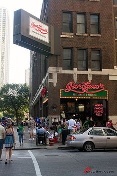 people are walking around in front of a restaurant on the corner of a city street