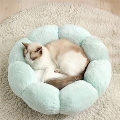 a cat curled up in a fluffy ball bed on the floor with its eyes closed