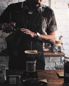 a man pouring coffee into a cup on top of a wooden table