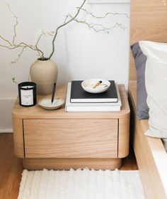 a table with a book, bowl and candle on it in front of a bed