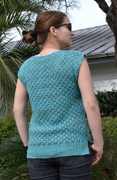 a woman standing in front of a tree with her back to the camera, wearing a blue knitted sweater