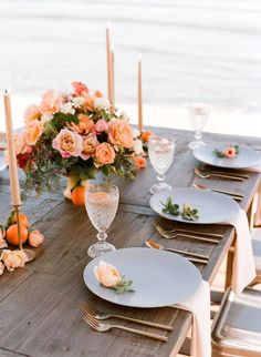 the table is set with white plates and silverware, peach flowers, candles, and greenery