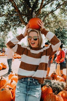 a woman standing in front of pumpkins with her hands on top of her head