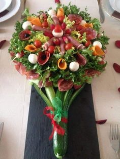 an arrangement of vegetables and meats on a black table cloth with red ribbon tied around it