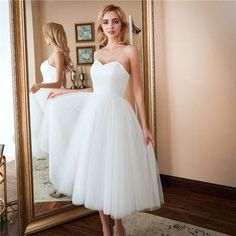 a woman standing in front of a mirror wearing a white dress