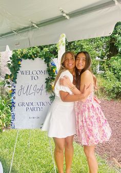 two women standing next to each other in front of a sign