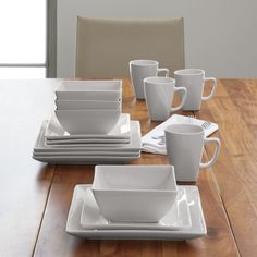 a wooden table topped with white dishes and cups