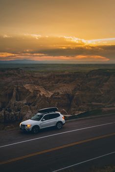 a white car driving down the road in front of some rocks and mountains at sunset