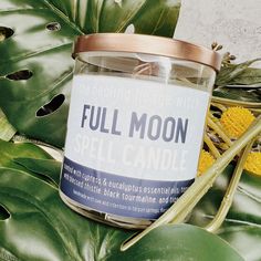 a candle that reads full moon on it next to some leaves and corn kernels