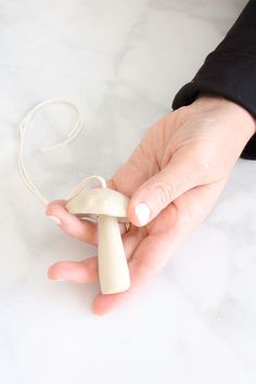 a hand holding an object in it's palm on a white surface with a string