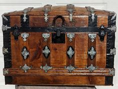 an old wooden trunk with metal decorations on the top and bottom, sitting in front of a white door