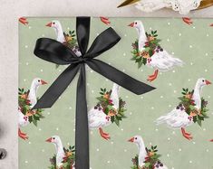 a gift wrapped in green wrapping paper with white geese and holly wreaths on it