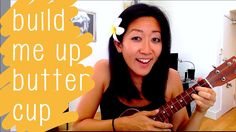 a woman is holding an ukulele in her hand and the words build me up butter cup are above her