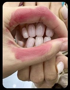 someone holding their hand over the mouth with pink lipstick on it's cheek and white teeth