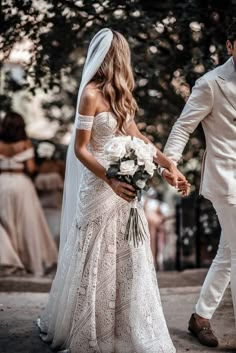 the bride and groom are walking down the street in their wedding attire, holding hands