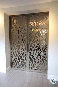 an intricately designed metal door in a white room with wood flooring and light colored walls