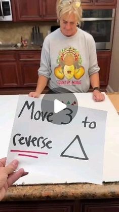 a woman sitting at a kitchen counter holding up a sign that says move 3 to reverse