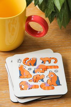 two coasters with orange cats on them next to a cup and plant in the background