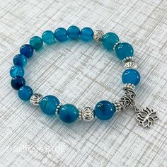 "Opt-in for a simple mediation bracelet with our Lotus Flower with Blue Agate Stones Bracelet. Agate will help you slow down and get centered. At the same time, the cerulean blue color soothing effect evokes feelings of peace and confidence. Add this bracelet to your daily wear accessories to keep calm throughout your day. The stones used in this piece are made from authentic agate stones with a refractive index of 1.530 to 1.543. The bracelet fits wrist sizes 5-9\". In addition, all our pieces Blue Agate Bracelets For Gifts, Adjustable Blue Crystal Bracelet For Meditation, Blue Agate Bracelet, Blue Spiritual Crystal Bracelet, Blue Lace Agate Bracelet, Blue Agate Stone, Cerulean Blue, Protection Bracelet, Tiger Eye Stone