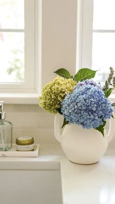 a white vase filled with blue and green flowers sitting on top of a kitchen counter