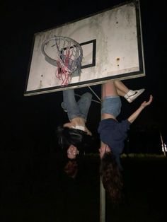 two girls hanging upside down on a basketball hoop