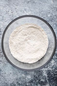 a glass bowl filled with flour sitting on top of a gray counter next to a knife