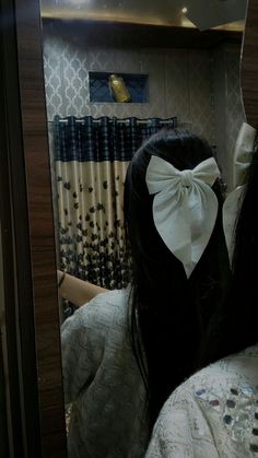 a woman with a white bow on her head looking at herself in the reflection of a mirror