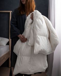 a woman is holding an unmade white jacket in her hands and standing next to a bed