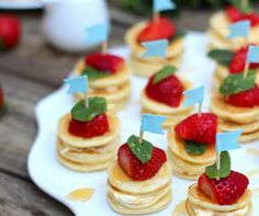 small pancakes with strawberries on them are arranged on a white plate and placed on a wooden table