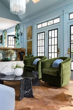 a living room with blue walls and green velvet chairs in front of a coffee table