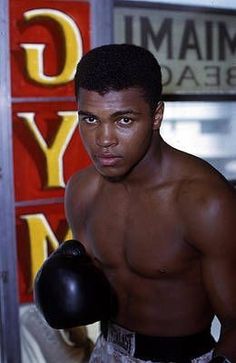 a shirtless man wearing boxing gloves in front of a gym sign