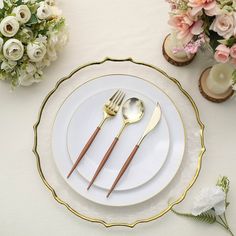 a white plate with gold trim and two forks on it next to some pink flowers