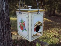 a bird house hanging from the side of a tree in front of some grass and trees