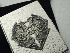 an ornate silver card case with flowers and vines in the shape of a heart on a black background