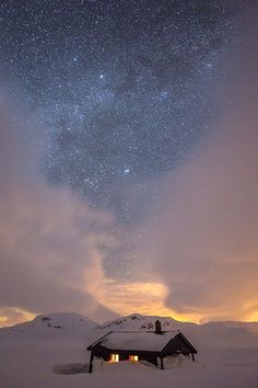 the night sky is filled with stars above a cabin in the middle of snow covered mountains