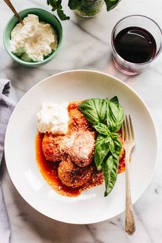 a white plate topped with meatballs covered in sauce and garnished with basil