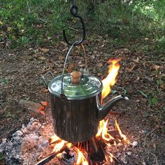 a tea pot sitting on top of a fire in the woods