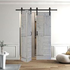 the interior of a living room with white walls and wooden floors, two doors open to reveal a bathroom