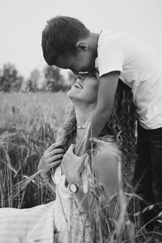 a man kissing a woman in the middle of a field with tall grass and trees