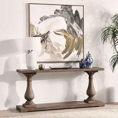 a table with two vases on it in front of a painting and potted plant