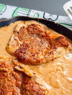 some kind of meat with gravy in a skillet on top of a table