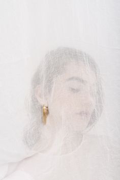 a woman's face is covered with white fabric and gold earring posts are in the foreground