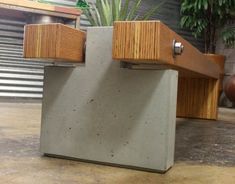 a concrete bench with wooden slats on the top and bottom, in front of a planter