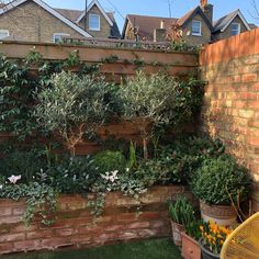 an outdoor area with plants and flowers in pots on the side of a brick wall