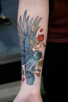 a blue bird with leaves and flowers on it's arm